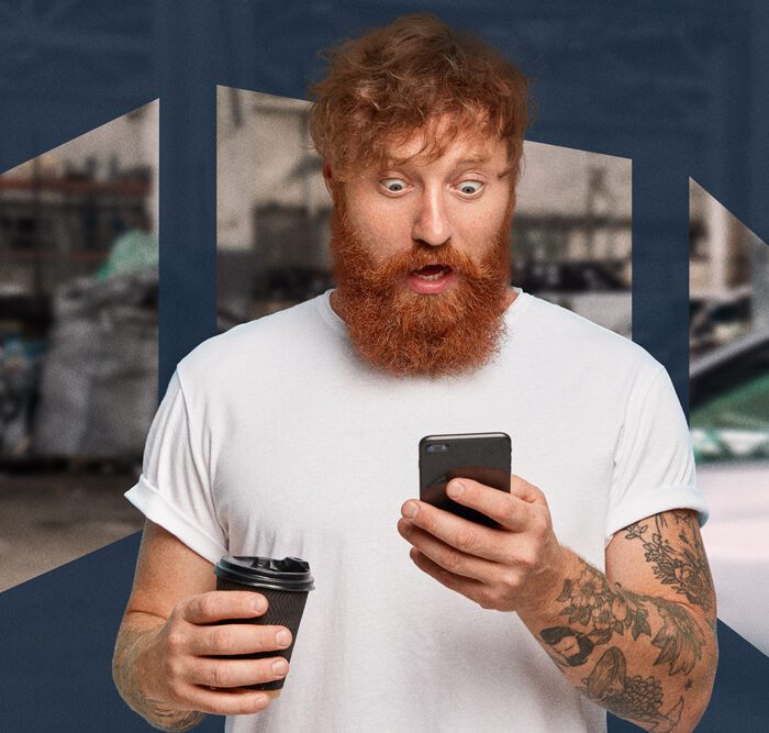 Man with red beard, eyes wide and mouth open, looking shocked at his phone while holding a coffee cup