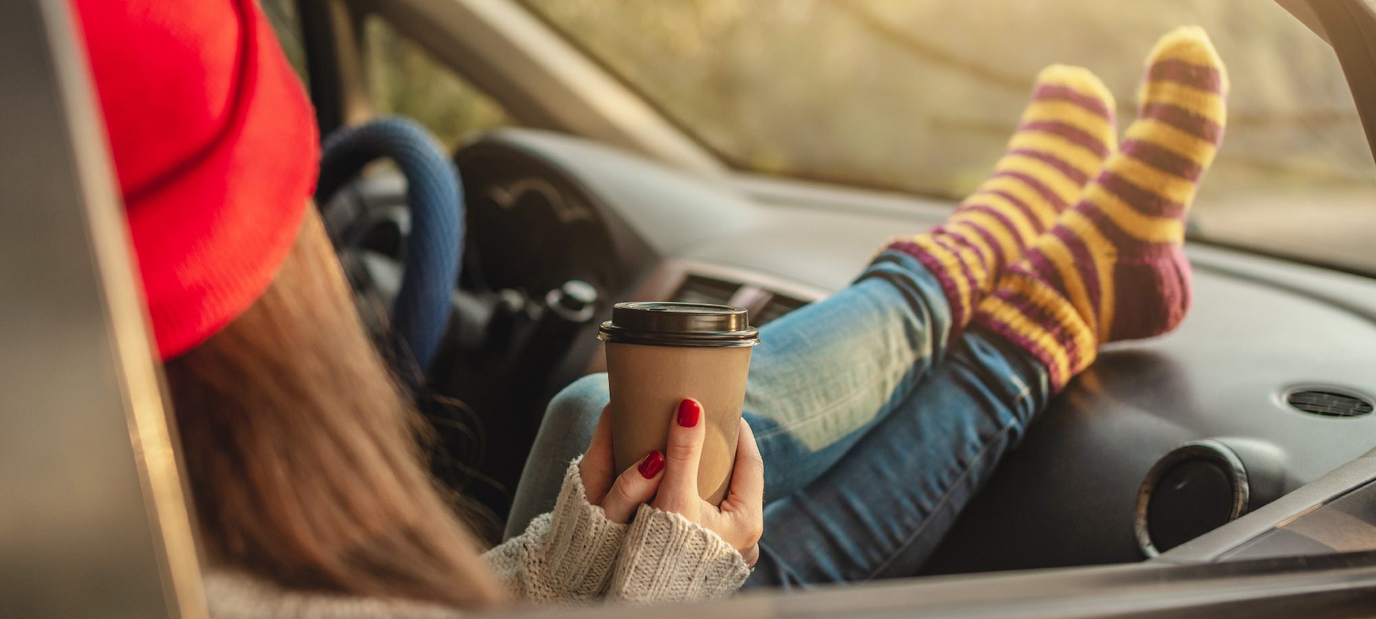 Woman sitting inside her car holding a cup of coffee