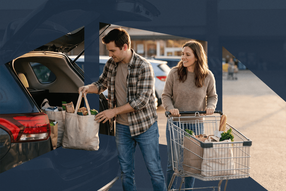 Man loading grocery bags into a car trunk as a woman stands beside a shopping cart