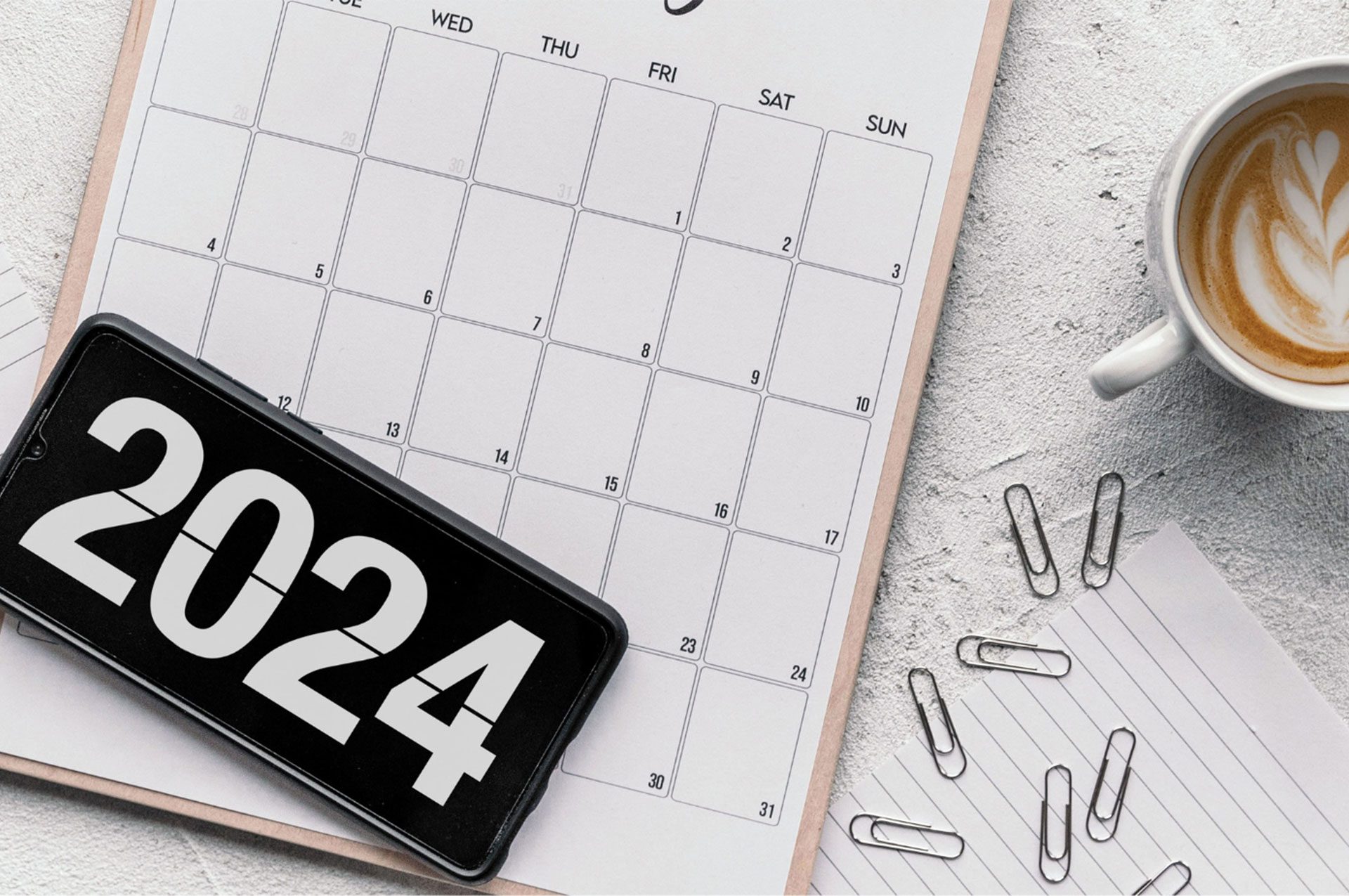 Calendar, 2024 image on cell phone screen, cup of coffee and paper clips resting on desk surface