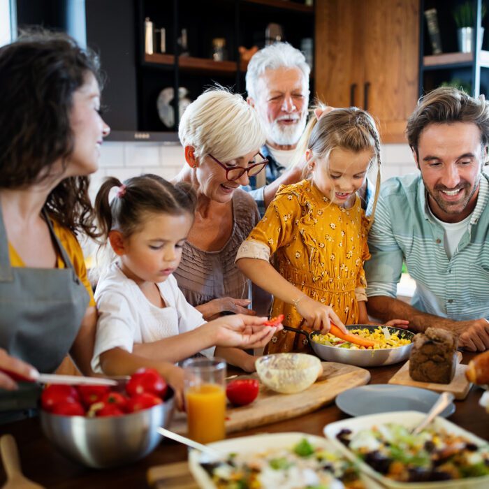 A joyful family gathers in a bright kitchen, preparing a meal together. Adults and children smile, slicing vegetables, with a cozy, warm atmosphere.