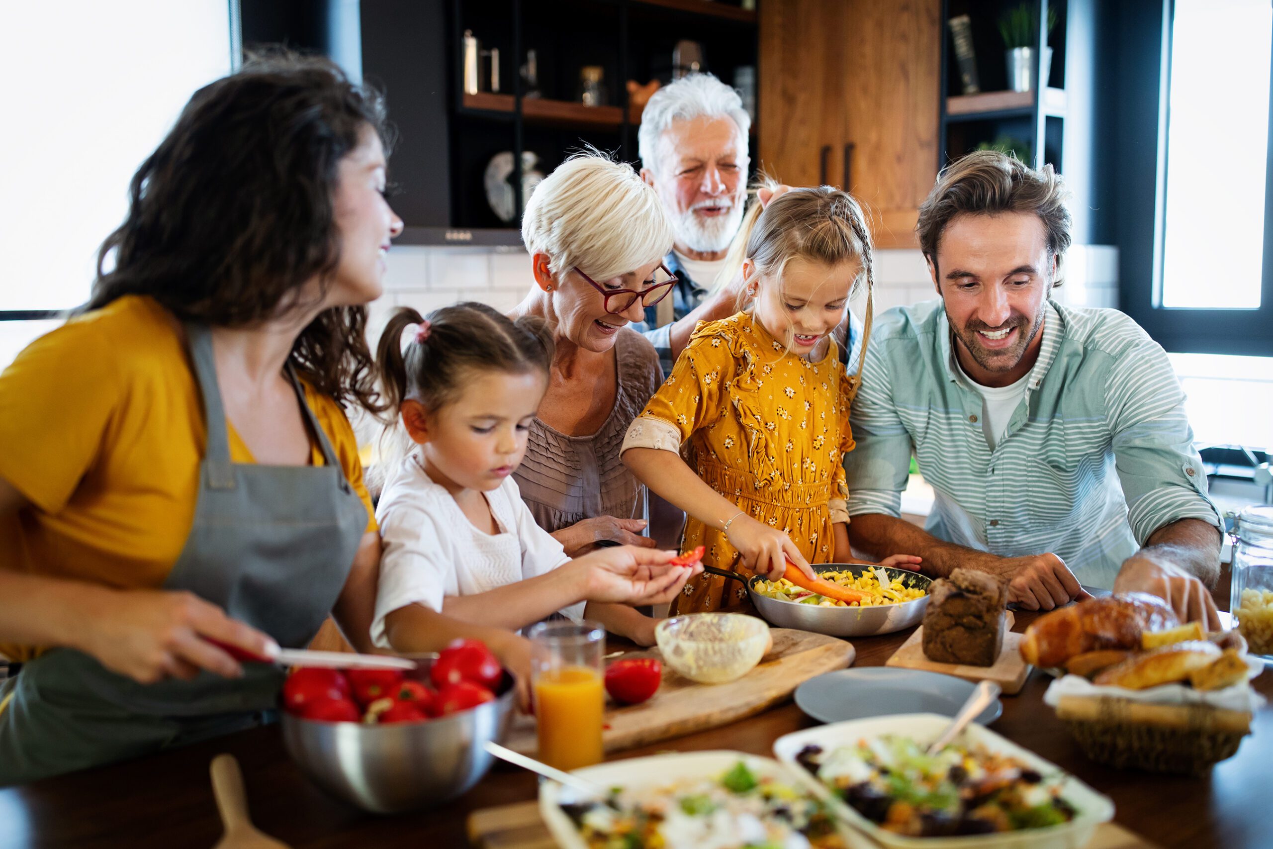 A joyful family gathers in a bright kitchen, preparing a meal together. Adults and children smile, slicing vegetables, with a cozy, warm atmosphere.