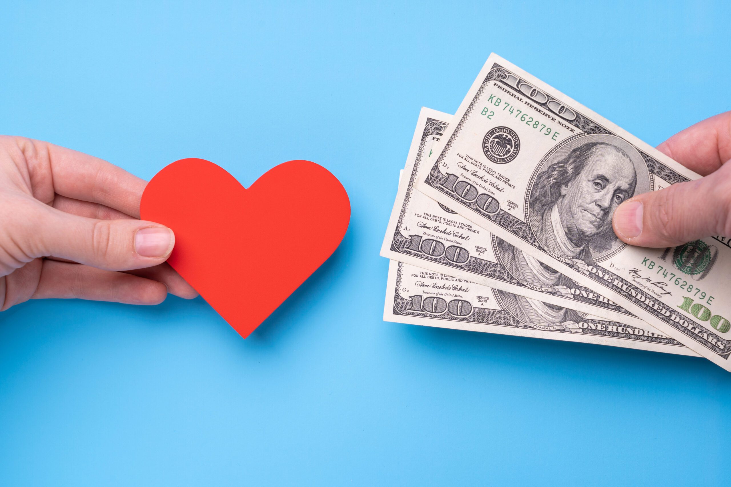 Male hand gives 300 dollars to female hand with red heart, blue background