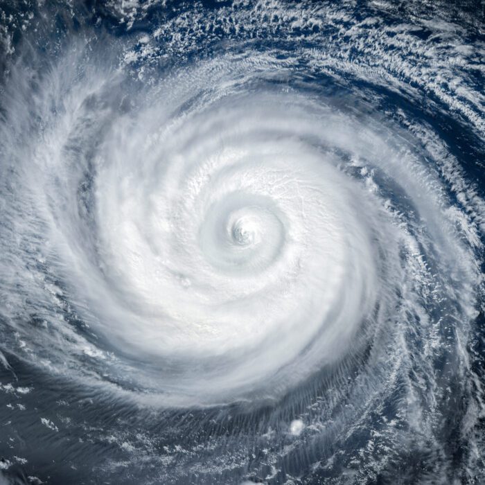 Satellite image of a massive hurricane with a well-defined eye in the center, swirling white clouds extending over dark blue ocean waters.