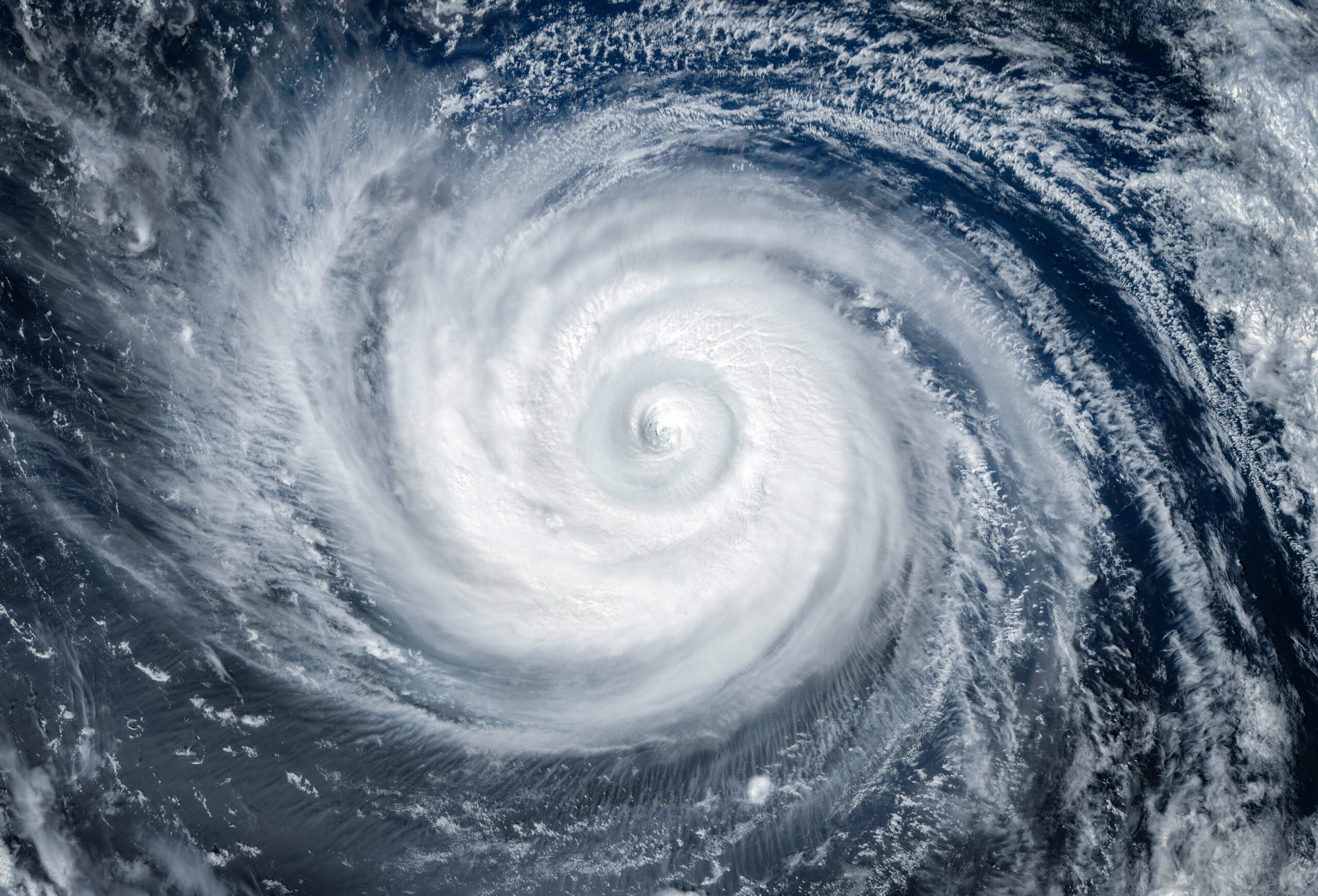 Satellite image of a massive hurricane with a well-defined eye in the center, swirling white clouds extending over dark blue ocean waters.