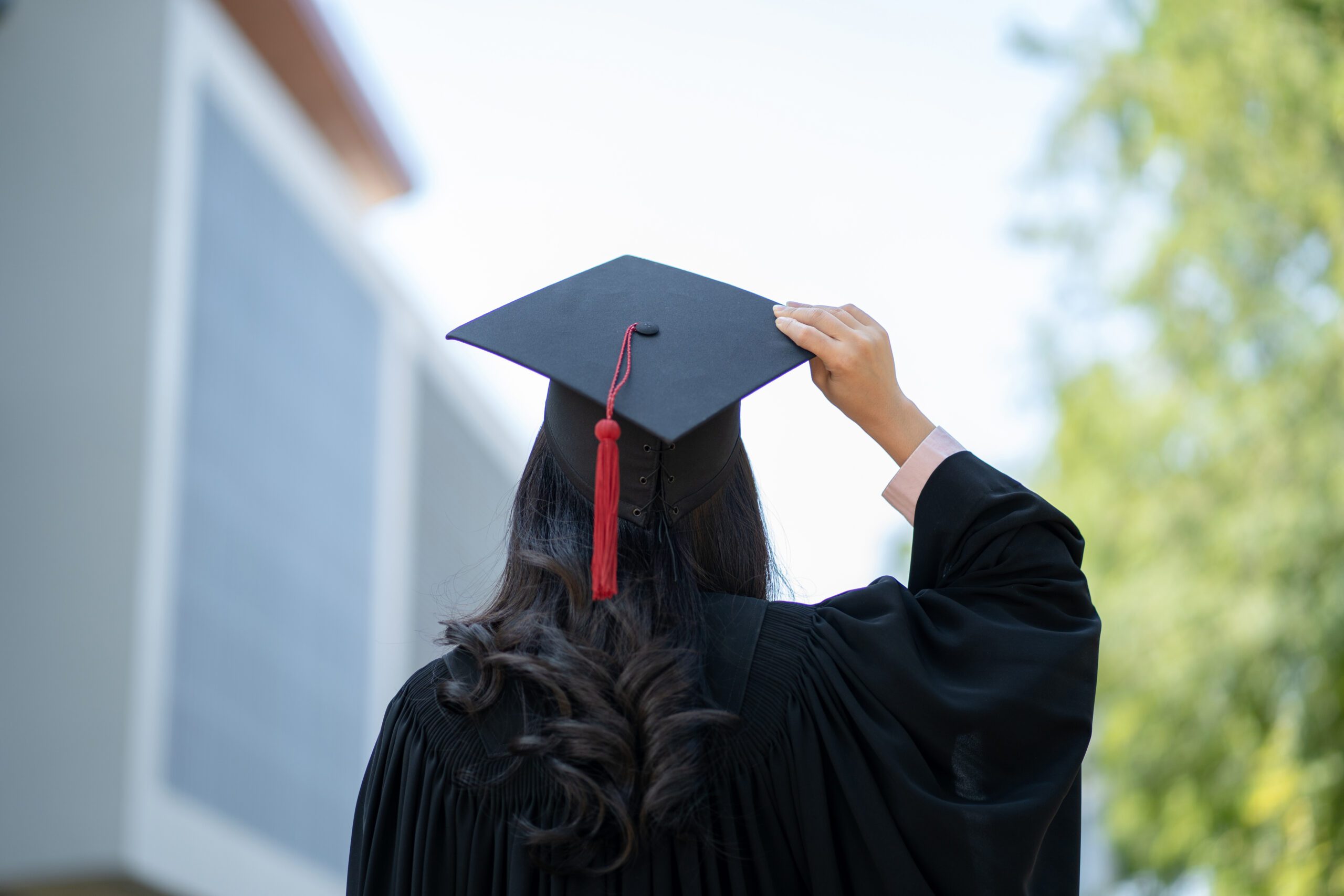 Graduation day, back view of Asian woman with graduation cap and coat holding diploma, success concept
