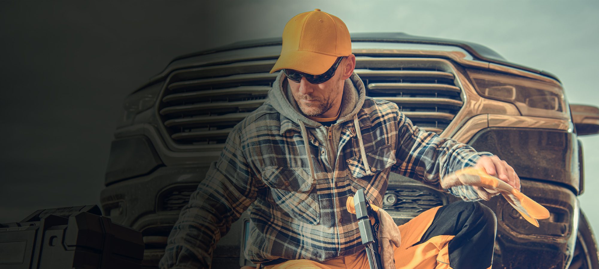 Man in work clothes and yellow cap holding gloves, with a truck in the background