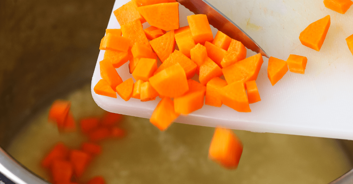 carrots being slid into an instant pot from a cutting board with a knife